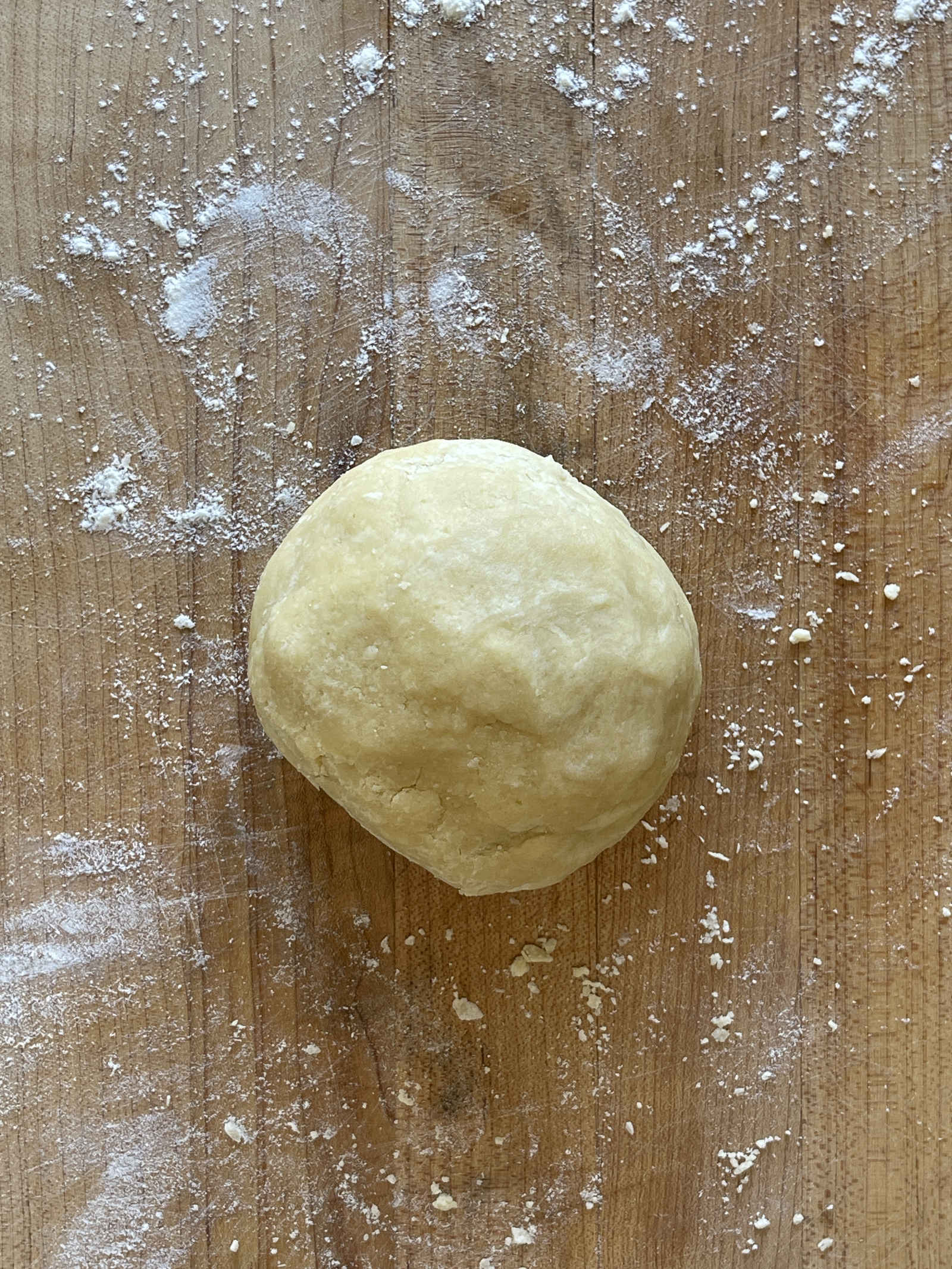 A ball of semolina pastry for one pie crust sits on a flour-dusted wooden cutting board