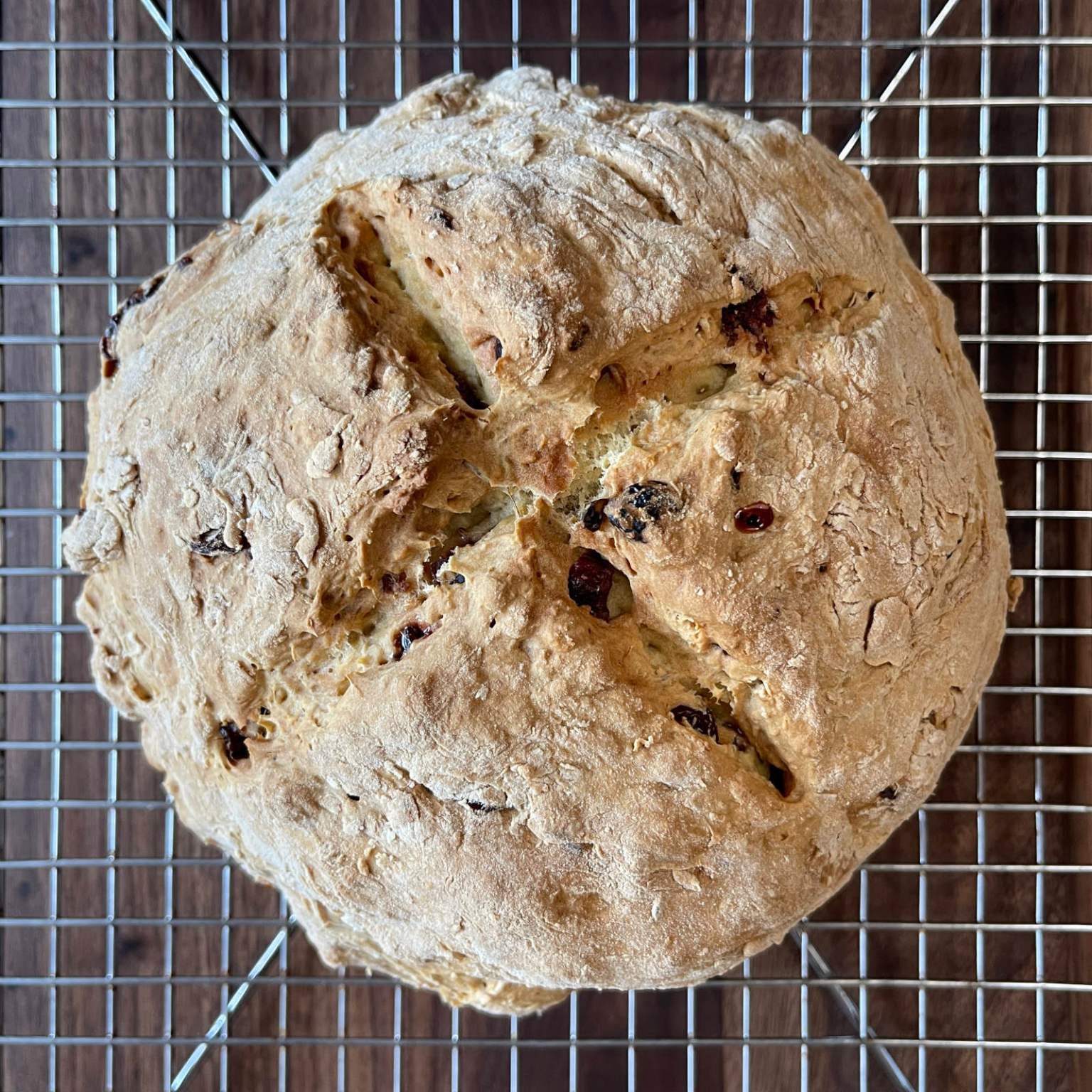 Vegan cranberry soda bread made with soy buttermilk cools on a wire rack sitting on a dark wooden cutting board.