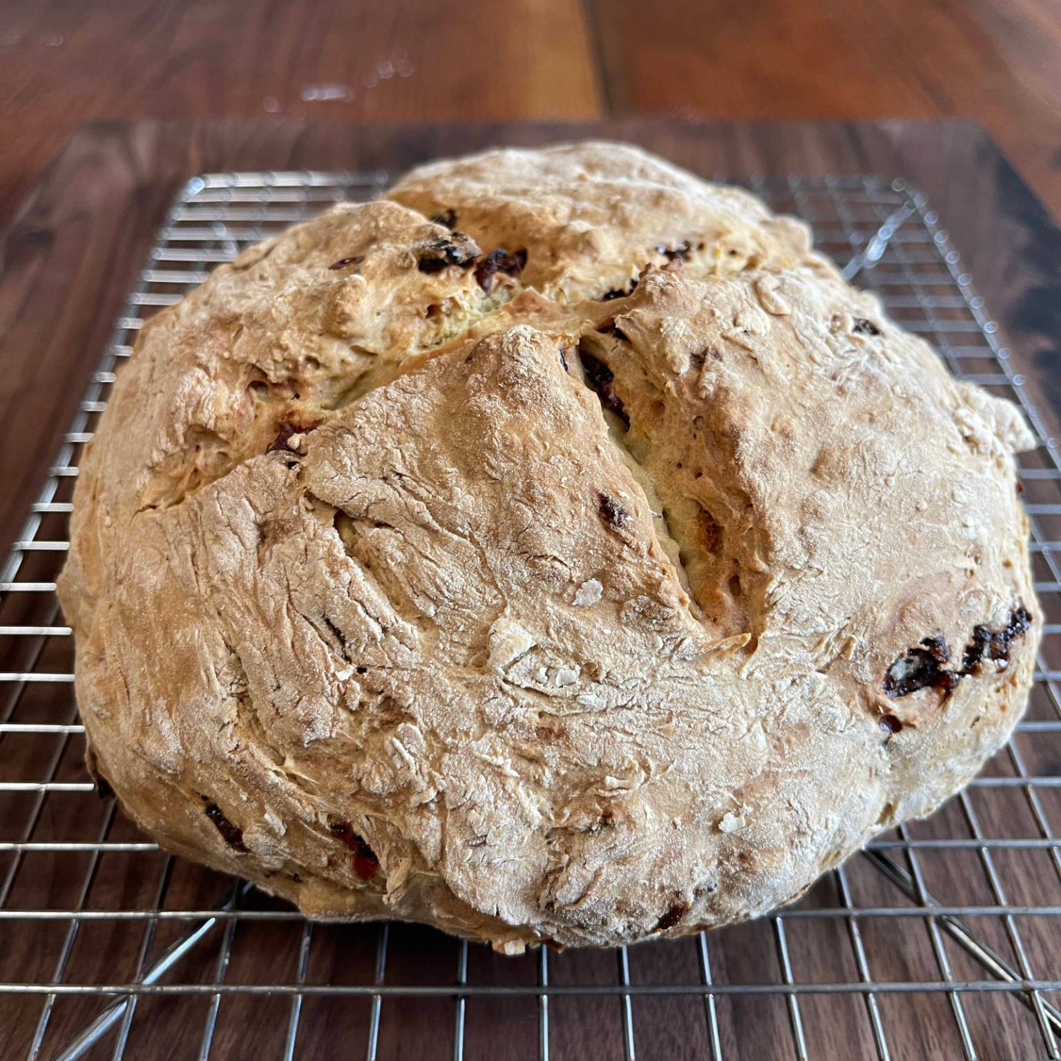 Vegan cranberry soda bread cools on a wire rack sitting on a dark wooden cutting board.