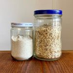 A smaller jar of oat flour (left) sits next to a larger flour of rolled oats (right)