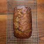 A loaf of coconut banana nut bread cools on a silver wire rack on a wooden background