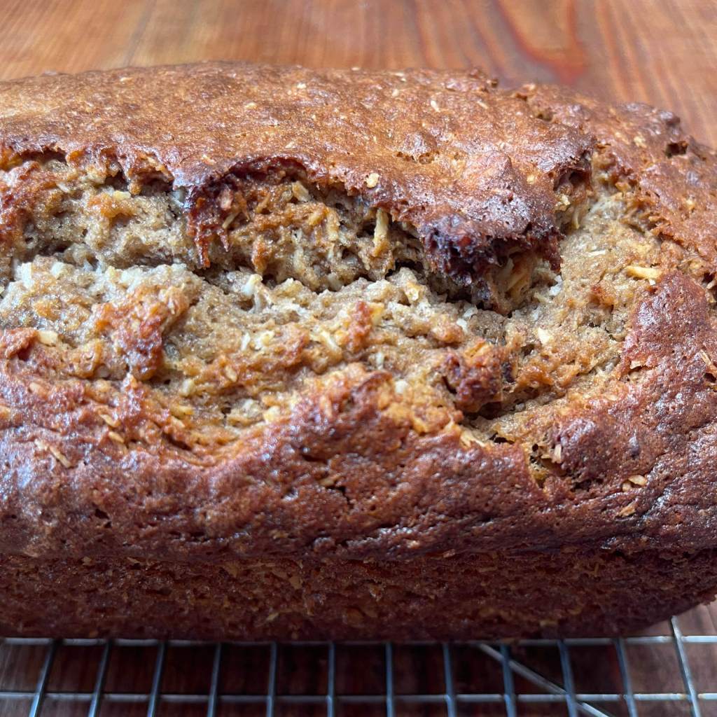 Closeup of a loaf of coconut banana nut quick bread cooling on a wire rack set on a wooden table