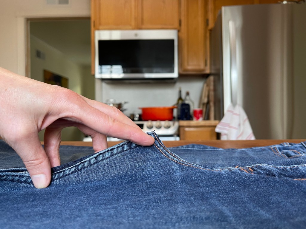 A hand holds up the curved inseam of a pair of jeans