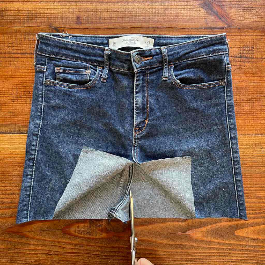 Scissors trim away the curved fabric of the seat of a pair of jeans. The legs have been removed.
