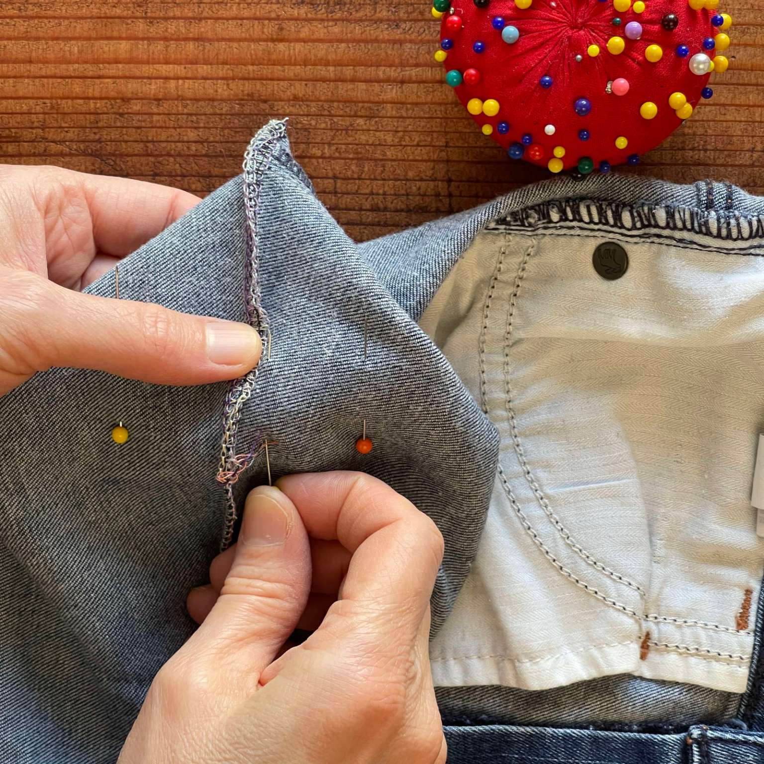 Hands pin one of the bottom edges of a denim shopping bag to sew a flat bottom