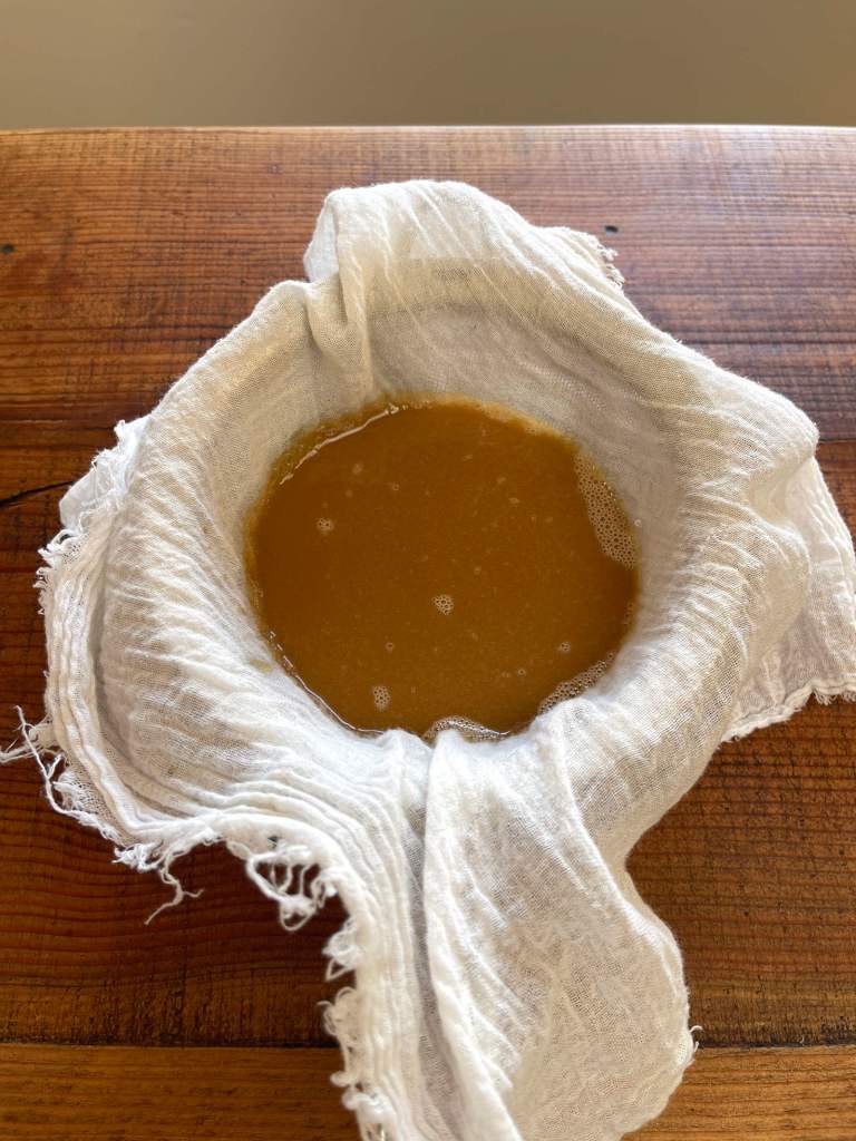 Homemade toasted sesame oil is straining through a cloth-lined sieve into a bowl