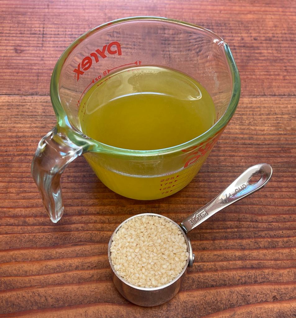 1 cup of avocado oil in a glass measuring cup and 1/4 cup of sesame seeds in a metal measuring cup sit on a dark wooden table