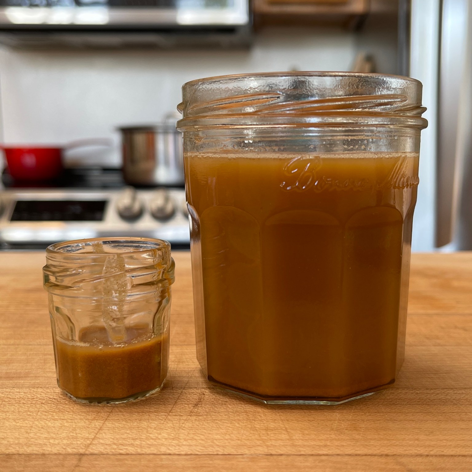 A large jar of toasted sesame oil and a small jar of toasted sesame seed pulp sit on a light colored wooden cutting board