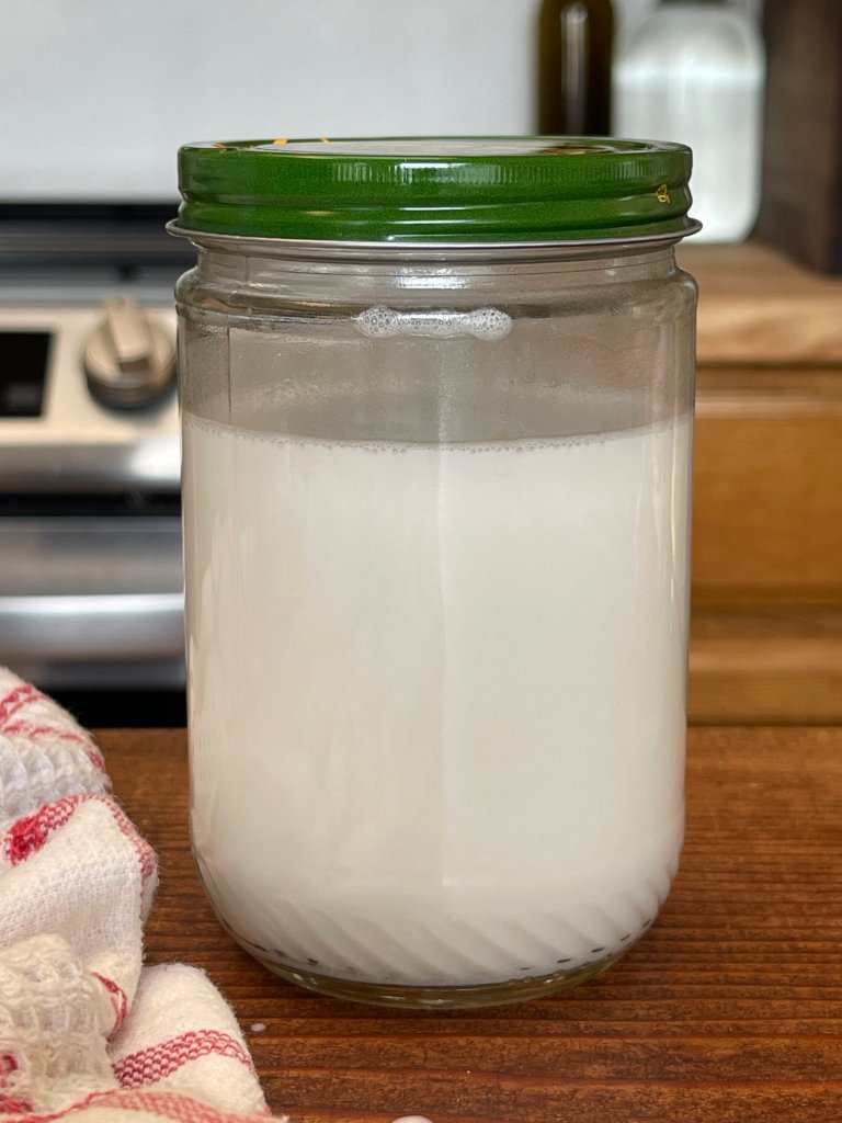 A jar of homemade coconut milk sits on a dark wooden table