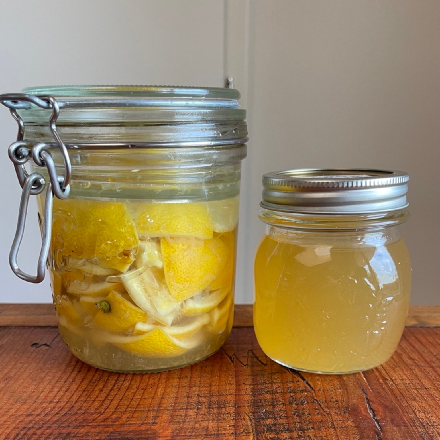 A jar of lemon rind soda at the start of fermentation sits on the left. A smaller jar of lemon rind syrup sits on the right.
