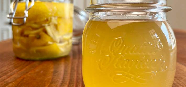 A jar of lemon rind syrup sits in the foreground. In the background in a jar of lemon rind soda at the start of fermentation.
