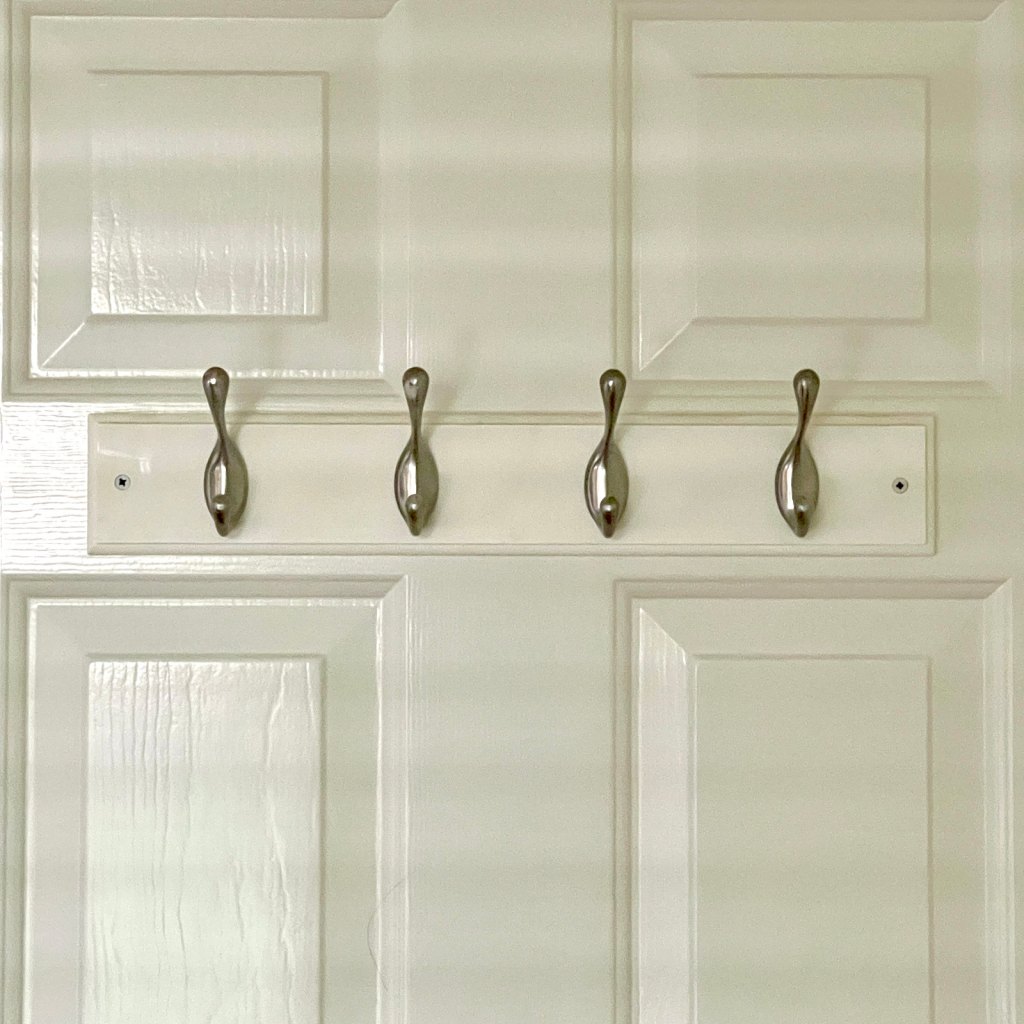 four silver clothing hooks on a white wooden mount attached to the back of a white door