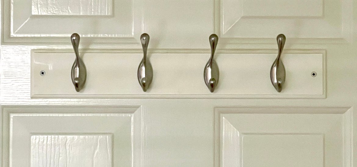 four silver clothing hooks on a white wooden mount attached to the back of a white door