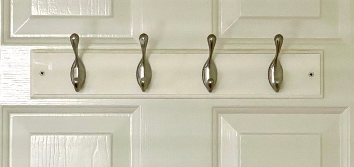 four silver clothing hooks on a white wooden mount attached to the back of a white door