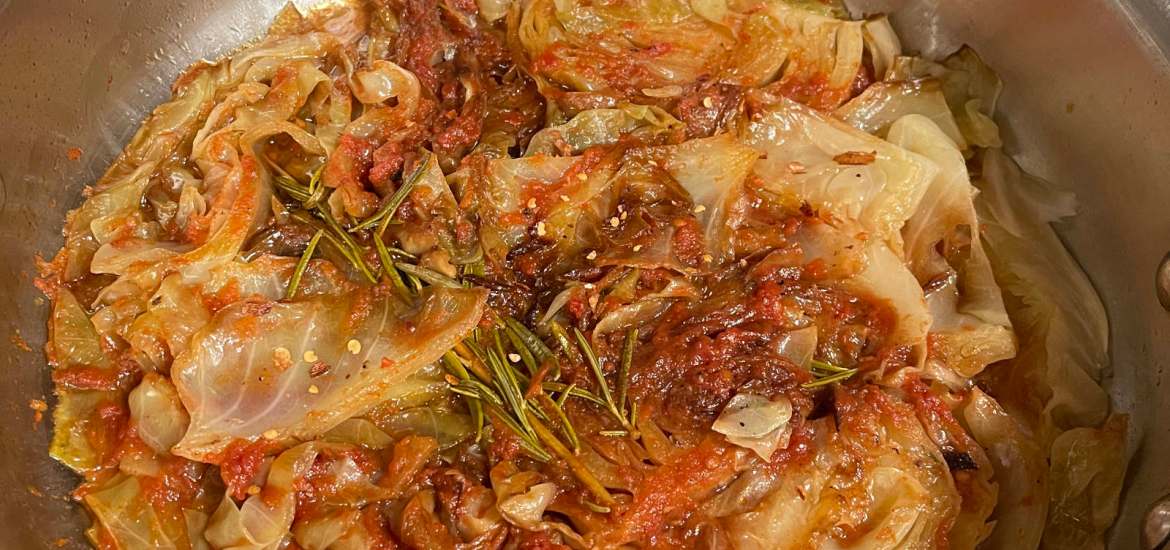 Braised cabbage cooking in a large, deep-sided, stainless steel skillet
