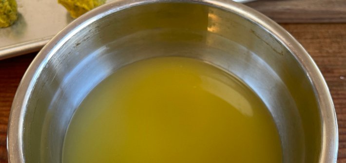 A stainless steel bowl of vegetable broth made from concentrated vegetables base. In the background are tablespoons of vegetable base on a silver cookie sheet.