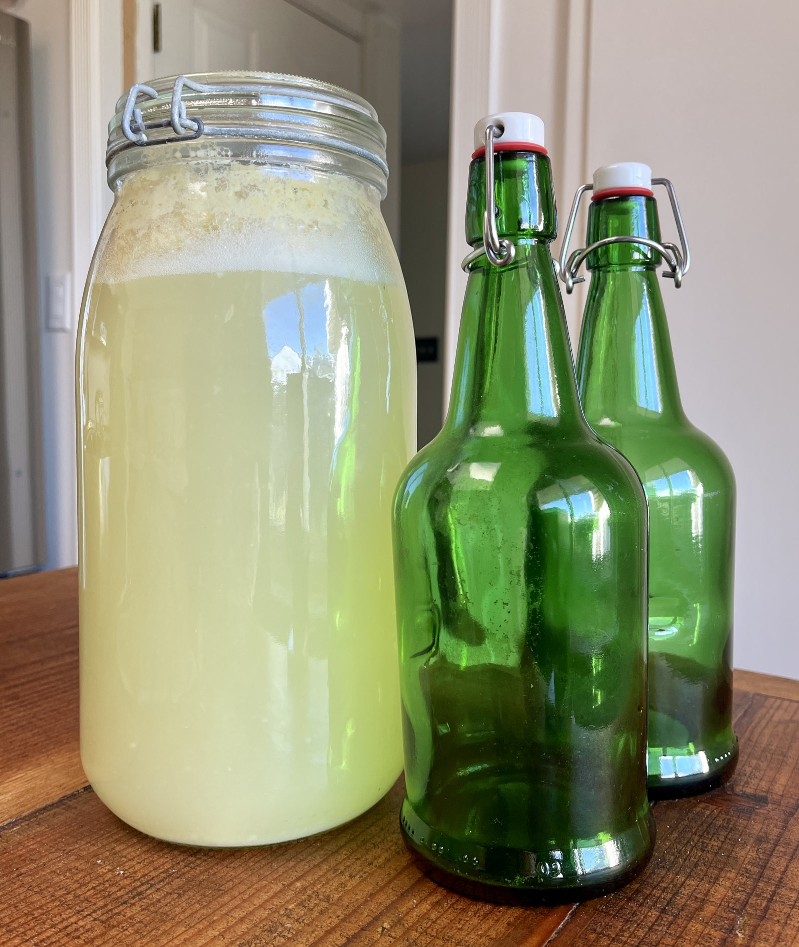 A large jar of carbonated lemonade sits next to two empty green flip-top bottles